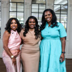 Photo of three African- American women smile and pose together at an elegant event venue