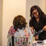 Photo of a healthcare professional in black scrubs takes a seated patient's blood pressure using a cuff and monitor at a health screening event.