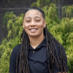Photo headshot of Reinvest Workforce Program Manager, Courtney Craig. African American Woman with long hair wearing a black collared shirt.