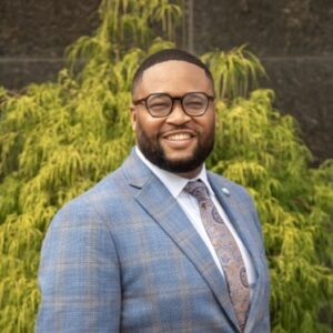 Photo Headshot of Reinvest Employment Relations Coordinator, Damion White. African American Man wearing glasses and a plaid suit.