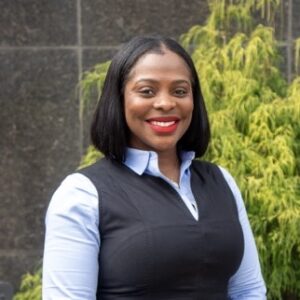 Photo headshot of Reinvest Program Manager, Jessica Pincham King. African American woman with shoulder-length hair wearing a blue collared shirt and black vest.