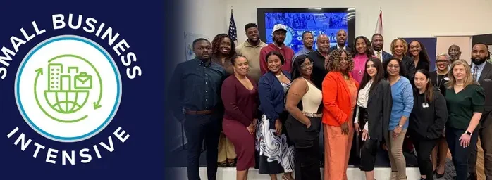A large, diverse group of smiling professionals posing together in a brightly lit room, positioned next to a blue graphic with the "Small Business Intensive" logo.