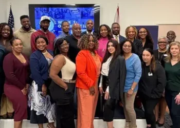 A large, diverse group of smiling professionals posing together in a brightly lit room, positioned next to a blue graphic with the "Small Business Intensive" logo.
